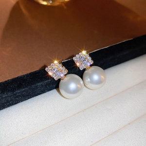 Macro shot of pearl drop earrings with gold base and sparkling zircon on black velvet