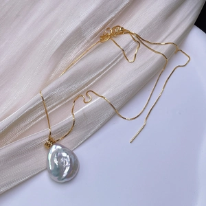 Baroque freshwater pearl necklace with gold chain and iridescent pendant on silk fabric