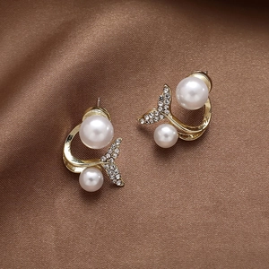 Close-up of golden fishtail earrings with pearls and crystals on brown satin fabric