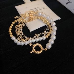 Detail of layered gold chain bracelet with white pearls and large OT buckle on black velvet