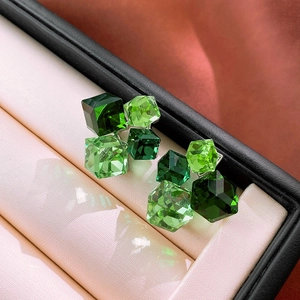Macro shot of emerald square crystal earrings with polished metal base in a jewelry box