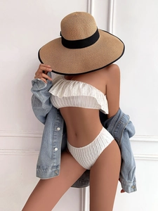 Detail of ruffled one-shoulder white bikini top paired with a light blue denim jacket