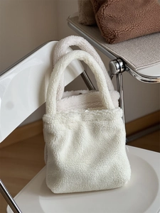 Close-up of white and beige faux fur tote bags on a chair showing soft texture