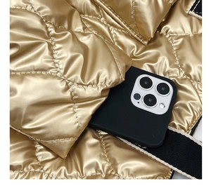 Detail of gold quilted padded crossbody bag showing glossy texture and size compared to phone
