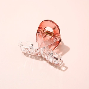 Close-up of a small pink gradient acetate hair claw clip on a soft pink background