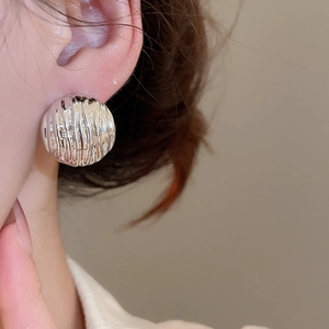 Macro view of a silver semi-spherical stud earring with textured ripple patterns