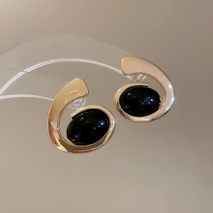 Close-up of gold irregular oval stud earrings with smooth black resin stone inlay