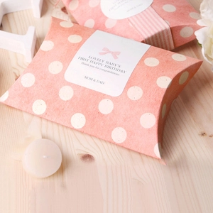 Pink polka dot paper pillow gift boxes with lovely baby birthday labels on wooden table