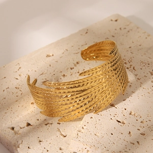Vue macro d'un bracelet manchette doré en plumes montrant les détails de texture ciselée
