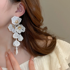 Macro detail of white woven flower tassel earrings with crystals on a female model