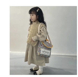 Detailed view of child wearing beige knit vest with floral blue crossbody bag