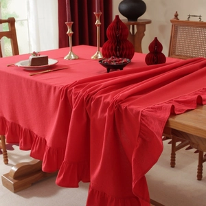 Detail of red cotton linen tablecloth featuring ruffled edges on a wooden dining table