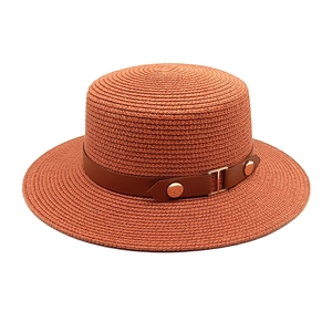 Detail of brick red straw boater hat with a brown leather band and gold metal buckle