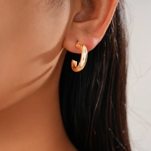 Close-up of a glossy gold C-shape hoop earring worn by a model for a minimalist metal look