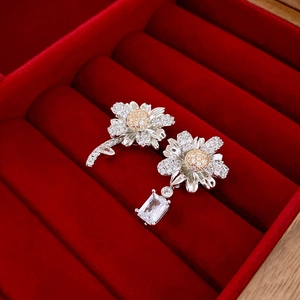 Detail of asymmetrical daisy silver earrings with crystals on a luxury red velvet box