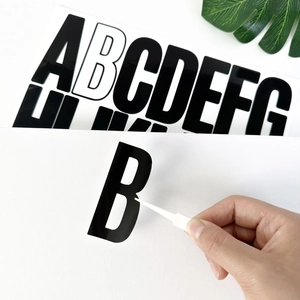 Close-up of tweezers peeling a black 3-inch uppercase letter B vinyl sticker for DIY decor