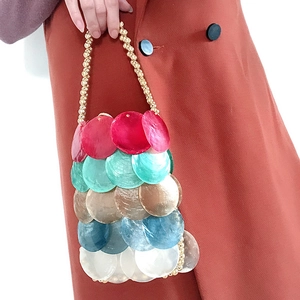 Handgefertigte bunte Pailletten-Handtasche mit Perlenkette vor dunkelrotem Mantel
