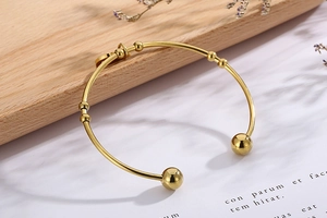 Detail of elegant gold stainless steel open bangle with bead and ball accents on paper