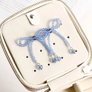 Detail of light blue beaded bow earring inside a white leather jewelry storage case