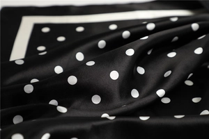 Detailed view of glossy black satin square scarf with white polka dot pattern textures