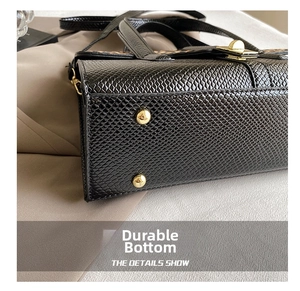 Close-up of black embossed faux leather bag bottom with four protective gold metal feet studs