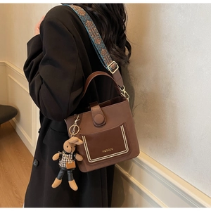 Detail of dark brown bucket bag with embroidered wide strap and cute bunny pendant