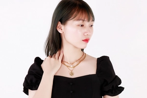 Détail du collier doré multicouche avec perle baroque et pendentif pièce de monnaie