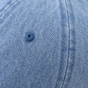 Detail of washed denim fabric showing reinforced stitching and embroidered eyelet on cap