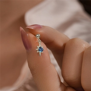 Macro shot of 925 silver star earring with blue zircon stone held by fingers