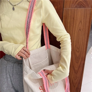 Detail view of canvas tote bag with woven jacquard strap and colorful pompom charms