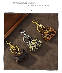 Three mini leopard print purse charms with gold and silver keychains on leather background