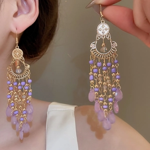 Close-up of golden tassel earrings with purple beads and teardrop gemstone on model