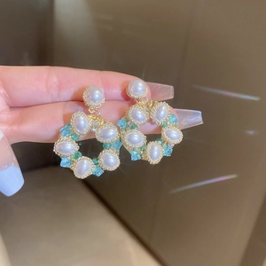 Detail of floral wreath earring with faux pearls and pastel crystals in a hand-held shot