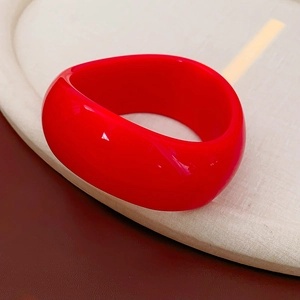 Close-up of a glossy red irregular wave resin cuff bracelet on a textured display