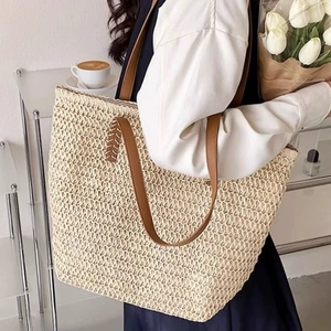 Close-up of minimalist beige straw tote bag with brown leather handles in a cozy home setting