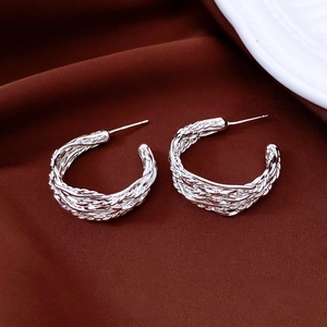 Détail de boucles d'oreilles créoles C tressées argentées sur fond en tissu bordeaux