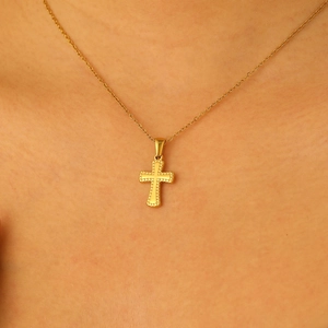 Close-up of gold cross pendant with textured finish on a layered metal chain necklace