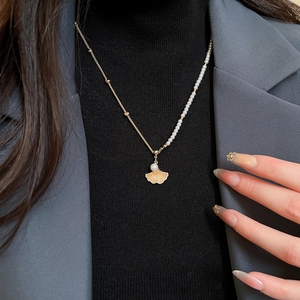 Detail view of asymmetric ginkgo leaf necklace with pearl and gold chain on model