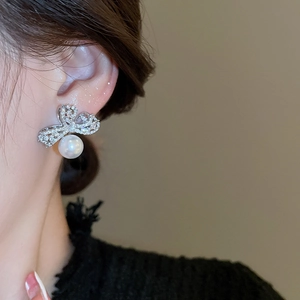 Close-up of silver bow earrings with zircon pavé and a hanging white pearl