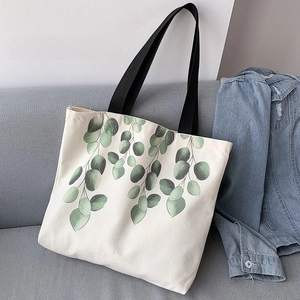 Detail of canvas tote bag featuring green leaf print and black woven handles on a sofa