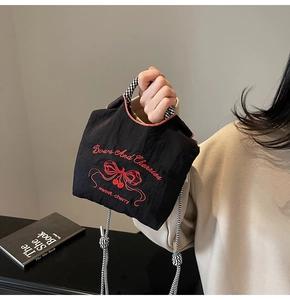 Close-up of black nylon handbag with red cherry butterfly embroidery and woven handles