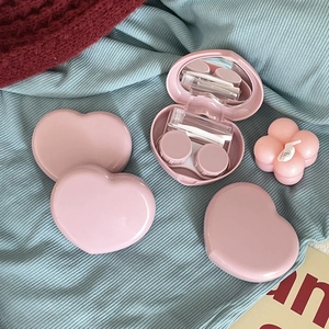 Detail view of pink heart contact lens case with mirror, tweezers, and applicator tool