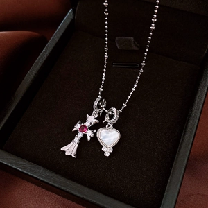 Detail of cross and heart pendant necklace with red zircon and white shell on velvet