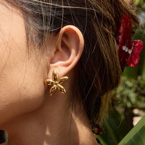 Detail of golden five-petal flower earring shown on model in natural outdoor light