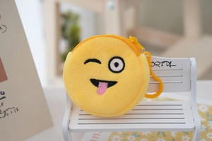 Detail of yellow plush cartoon coin purse with embroidered emoji wink and tongue on a bench