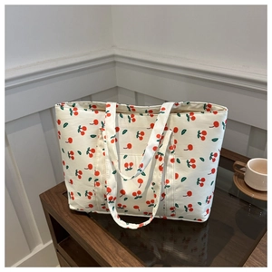 Close-up of cream quilted tote bag with red cherry print on dark wooden table