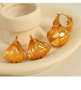 Close-up of golden shell-shaped and wide hoop earrings on a ceramic dish