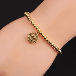 Close-up of a gold-plated beaded bracelet featuring a classic smiley face charm on wrist