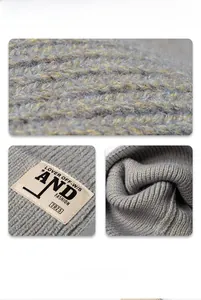 Gros plan sur la maille torsadée grise et l'écusson beige de ce bonnet d'hiver tendance