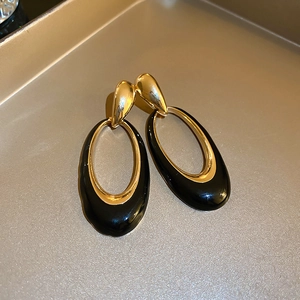 Detail of vintage oval drop earrings with golden metal finish and black enamel drip